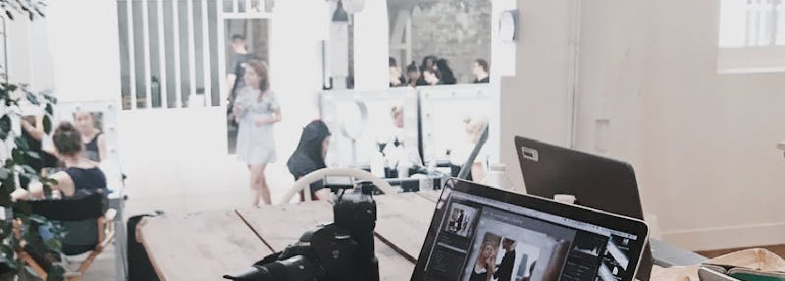 A bright, modern workspace featuring laptops, a camera, and a drawing tablet in an indoor office.